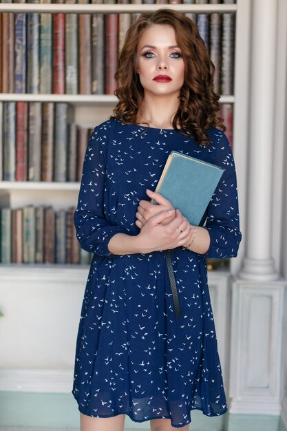 Belle jolie fille en robe de cocktail gaine bleue posant dans l'intérieur de la bibliothèque de luxe