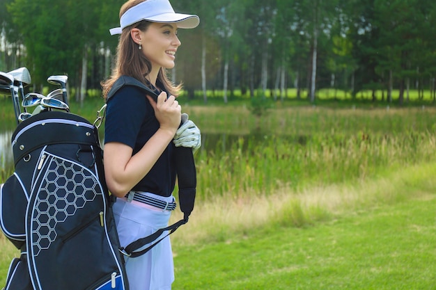 Belle joueuse de golf portant un sac de golf et souriant.