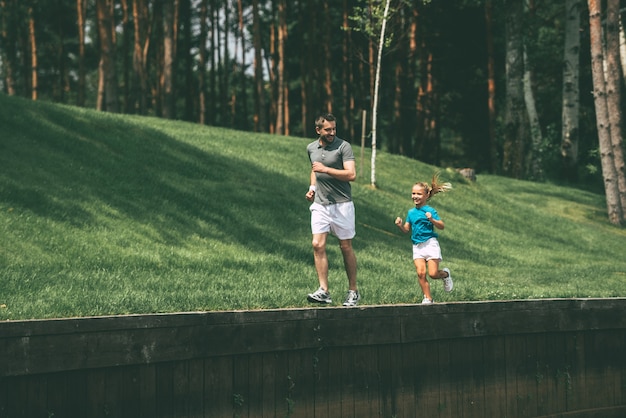 Belle journée pour faire du jogging. Toute la longueur du joyeux père et fille faisant du jogging ensemble dans le parc