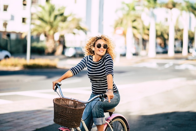 Belle et joyeuse jeune femme adulte profite d'une balade à vélo dans une activité de loisirs de plein air urbaine ensoleillée dans la ville - portrait de gens heureux - femme branchée à l'extérieur s'amusant