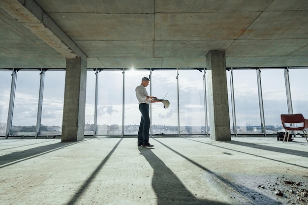 Belle lumière du soleil passe à travers une grande fenêtre Jeune homme en tenue de soirée travaille à l'intérieur sur la construction