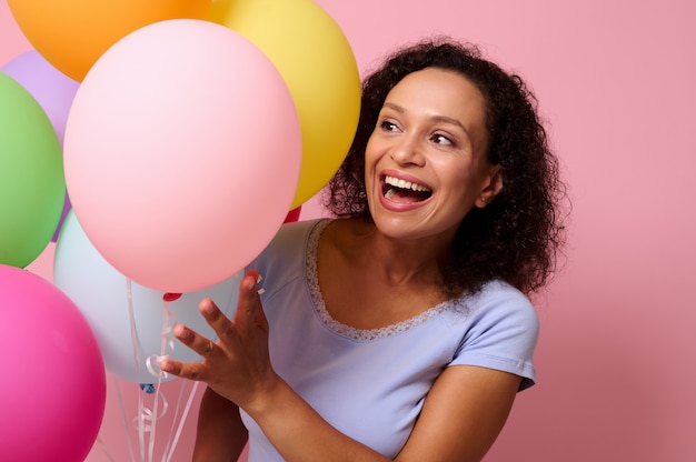 Belle magnifique femme gaie superbe attrayante mignonne souriante avec un beau sourire à pleines dents regardant à travers des ballons à air lumineux gonflés posant sur un fond de couleur rose avec un espace pour le texte