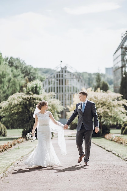 Belle magnifique mariée et le marié posant dans un parc de printemps ensoleillé parmi les feuilles vertes couple de mariage heureux marchant dans le jardin vert concept de fugue de moments de mariage heureux