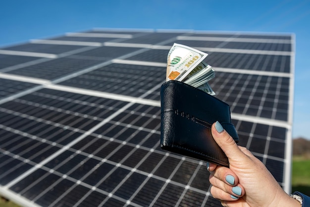 Belle main féminine tient un portefeuille noir avec des billets d'un dollar qu'elle tient près du soleil concept d'entreprise d'électricité verte achat de panneaux solaires