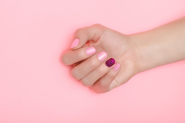 Belle main féminine avec un vernis à ongles rose parfait avec un nail art fleur rose sur une surface rose.