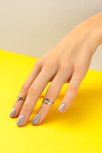 Belle main de femme avec un design d'ongle brillant sur gris et jaune