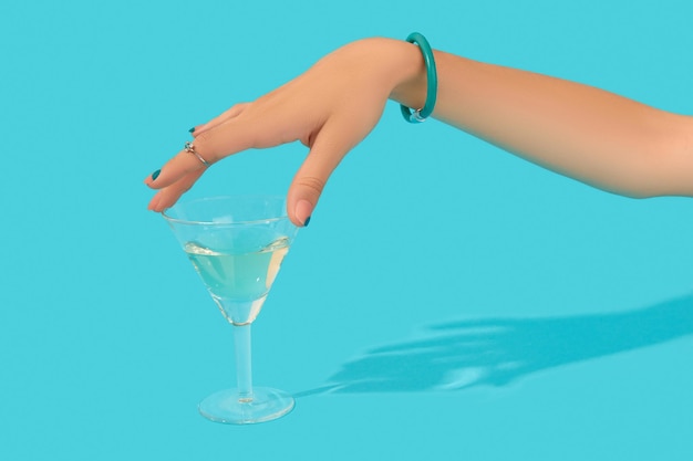 Belle main de femme soignée avec un verre de cocktail tactile à la mode sur fond bleu