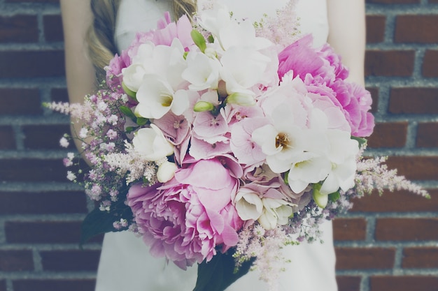 Belle mains de mariée tenant beau bouquet rose printanier. Mur de brique Fond. Toning.