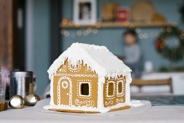 Une belle maison en pain d'épice avec un glaçage en gros plan se dresse sur la table de la cuisine