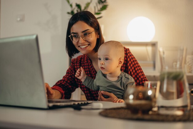 Photo belle maman d'affaires utilisant un ordinateur portable et passant du temps avec son petit garçon à la maison