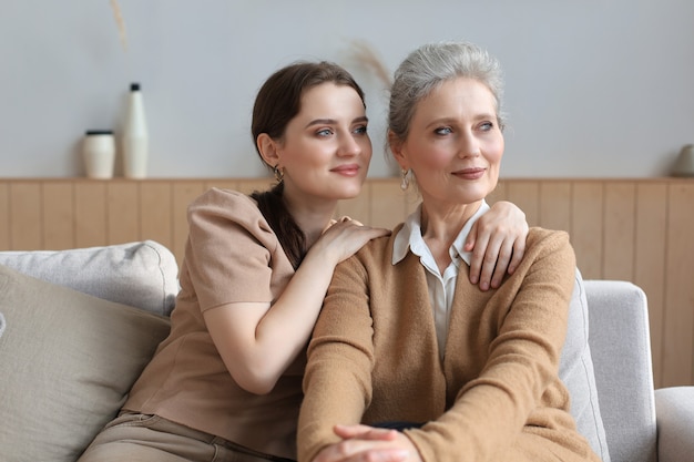 Belle maman d'âge moyen et sa fille adulte s'embrassent, regardent ailleurs et sourient.