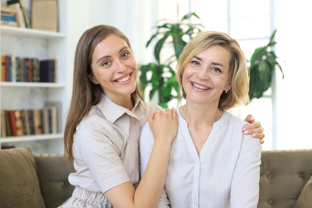 Belle maman d'âge moyen et sa fille adulte s'embrassent, regardent la caméra et sourient.