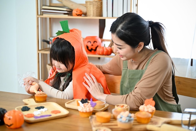 Belle maman asiatique apprenant à sa petite fille à faire un cupcake d'Halloween dans la cuisine