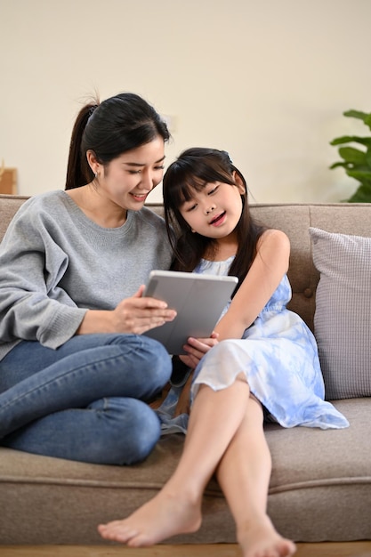 Belle maman asiatique regarde des vidéos ou joue à un jeu avec sa fille sur tablette