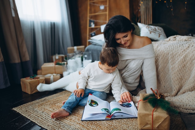 Belle maman aux cheveux bruns et beau garçon fils assis sur le sol et lisant un livre de contes de fées