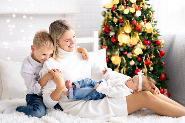 Belle maman avec deux enfants célèbre les vacances de Noël à la maison avec un arbre de Noël