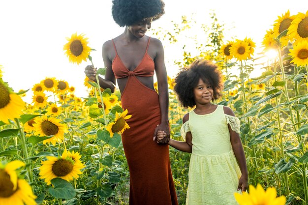 Belle maman et fille afro-américaines jouant et s'amusant dans un champ de tournesols