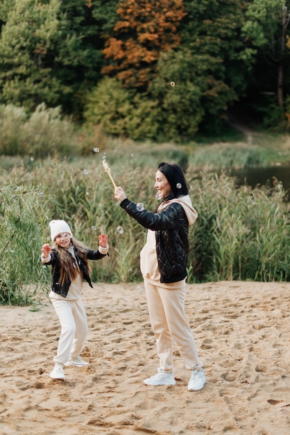 Belle maman et fille jouent et soufflent des bulles dans le parc d'automne