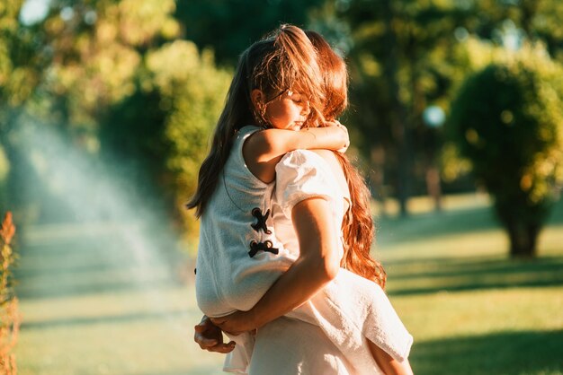 Belle maman tient et caresse sa douce petite fille dans ses bras à l'extérieur Joyeuse maternité Belle maman et son enfant jouant ensemble dans le parc Portrait de famille heureuse Joie de la fête des mères