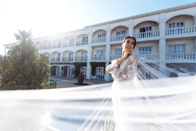 Belle mariée aux cheveux noirs en robe de mariée luxueuse posant sur un balcon avec vue sur la mer