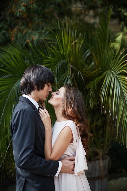 Belle mariée aux longs cheveux bouclés et marié debout près de l'autre à feuilles vertes, photo de mariage, beau couple, jour de mariage.