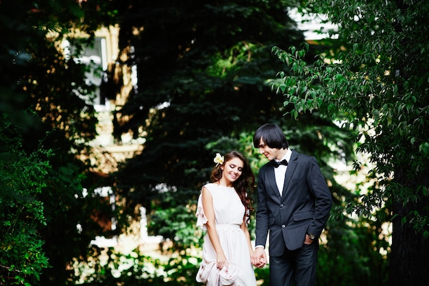 Belle mariée aux longs cheveux bouclés et marié debout près de l'autre à fond de feuilles vertes, beau couple, jour de mariage, gros plan portrait.