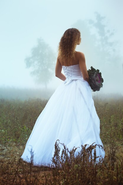 Belle mariée avec un bouquet sur un champ brumeux