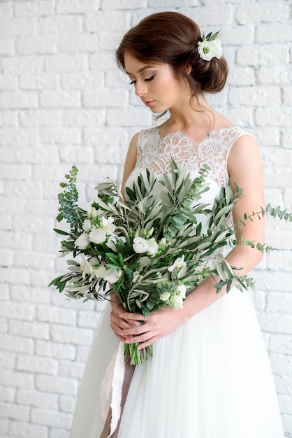 Belle mariée avec bouquet de fleurs. brune sur un mur de briques blanches fauves