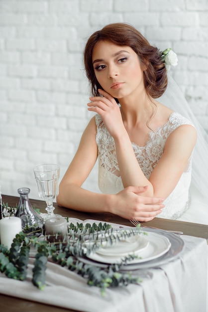 Belle mariée avec bouquet de fleurs. brune sur un mur de briques blanches fauves