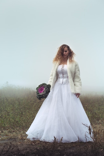 Belle mariée avec un bouquet sur fond de champ brumeux