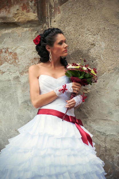 Belle mariée avec bouquet de mariée dans ses mains appuyé contre le mur d'un immeuble ancien