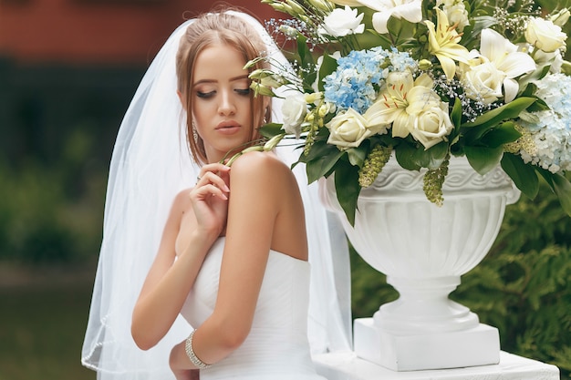 Belle mariée dans une magnifique robe de mariée posant parmi la verdure dans la rue. Concept de mariée pour les robes publicitaires