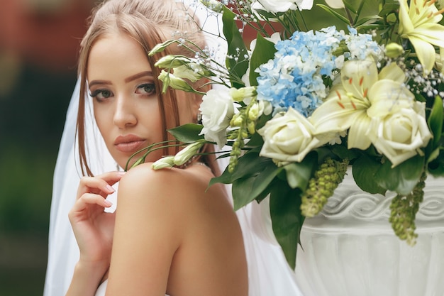 Belle mariée dans une magnifique robe de mariée posant parmi la verdure dans la rue