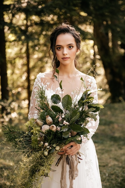 Belle mariée dans une robe blanche avec un bouquet sur un fond de forêt