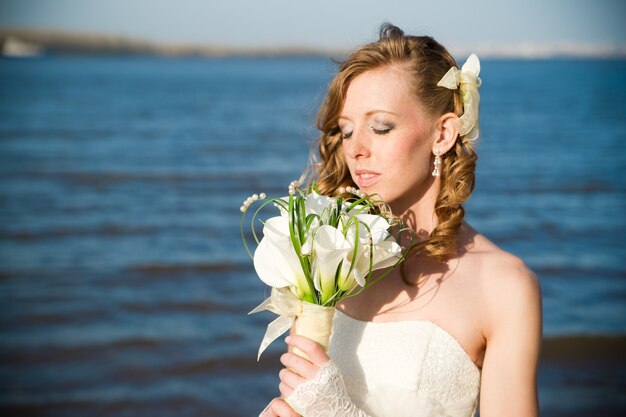 Belle mariée dans une robe blanche sur la côte de la rivière en été Maquillage et coiffure professionnels