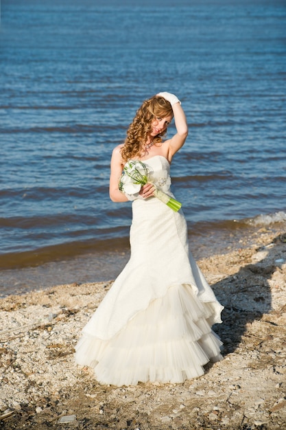 Belle mariée dans une robe blanche sur la côte de la rivière en été