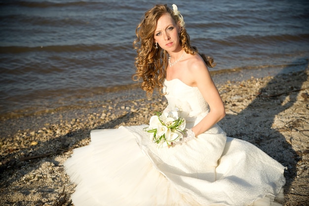 Belle mariée dans une robe blanche sur la côte de la rivière en été