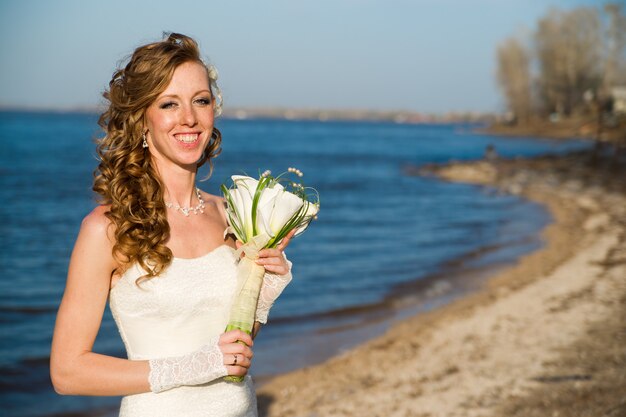 Belle mariée dans une robe blanche sur la côte de la rivière en été