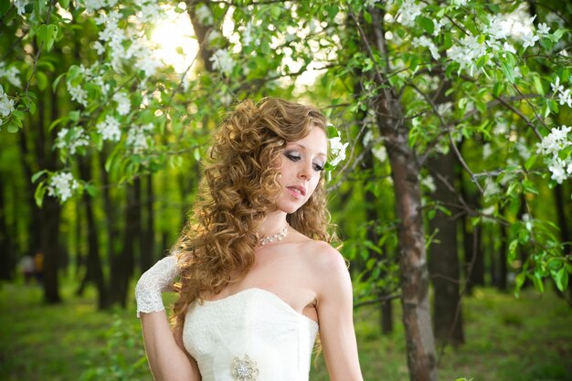 Belle mariée dans une robe blanche dans les jardins fleuris au printemps