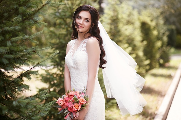 Belle mariée dans une robe de mariée blanche tenant un bouquet de roses