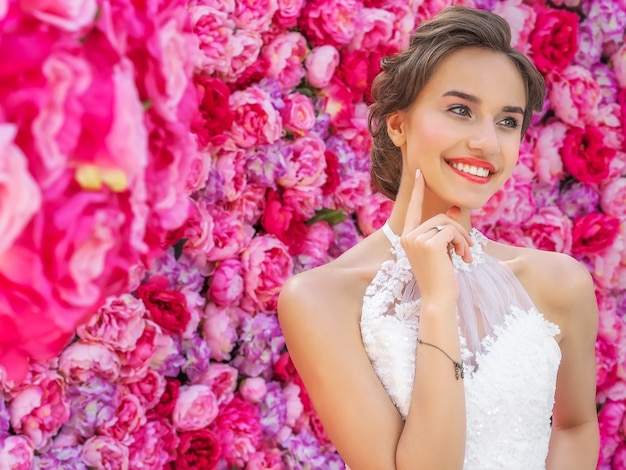 Belle mariée dans une robe de mariée posant avec des fleurs décoratives roses