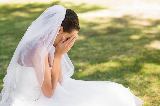 Belle mariée inquiète assis au parc