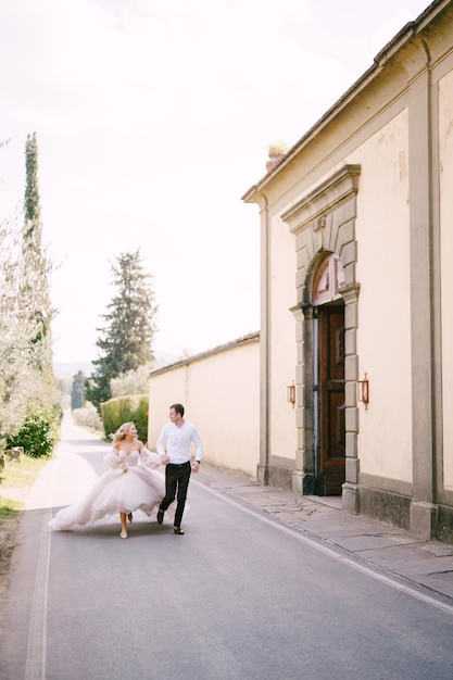 Belle mariée et le marié courant main dans la main à l'extérieur de la vieille villa en italie en toscane près de