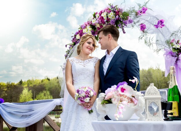 Belle mariée et le marié debout sous une arche florale à la journée ensoleillée