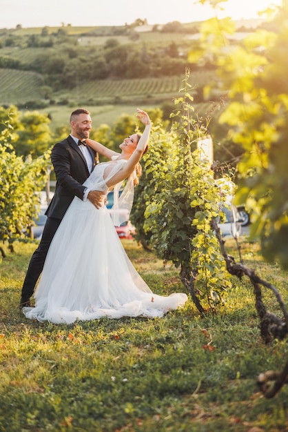 Une belle mariée et un marié heureux dansant dans le vignoble au coucher du soleil le jour de leur mariage.