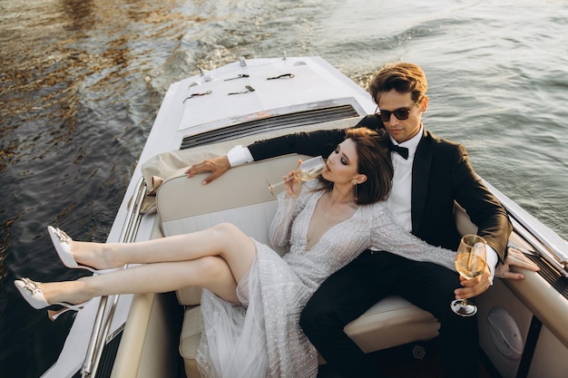 La belle mariée et le marié montent sur un yacht, boivent du vin et profitent du moment Jour du mariage