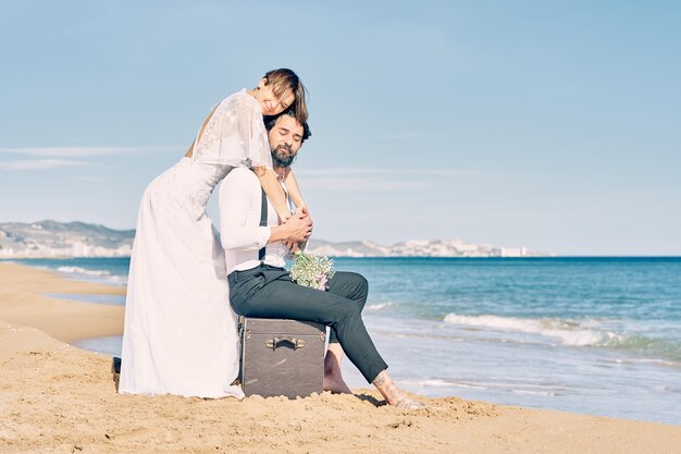 Belle mariée et le marié sur la plage s'embrassant en robes de mariée