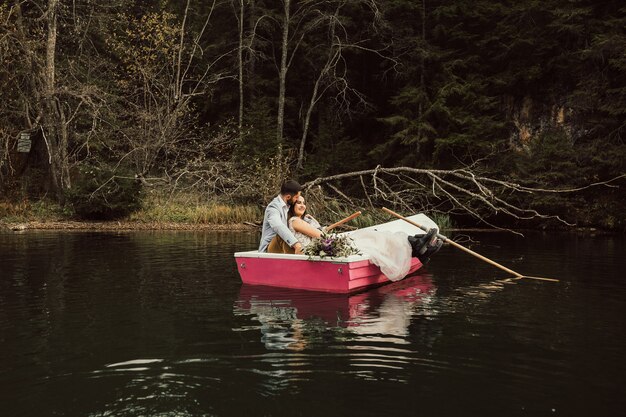 Belle mariée et le marié s'assoient ensemble dans un bateau rose sur le lac.