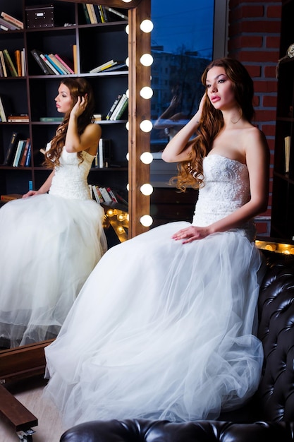 Une belle mariée portant une robe de mariée assise devant le miroir