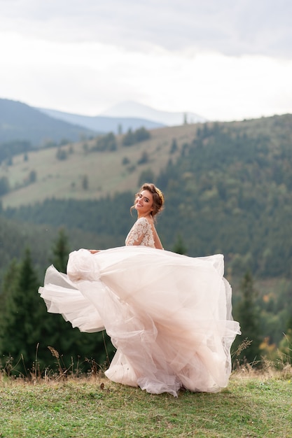 Belle mariée posant dans sa robe de mariée sur fond de montagnes.